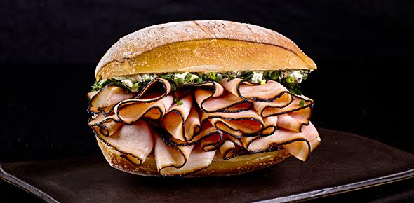 um sanduíche com tempero verde e fatias de presunto sobre um prato preto